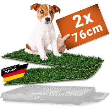Welpe auf zwei Kunstrasenauflagen über einer Schale, oranges Schild „2x 76cm“, Etikett mit Deutschland-Flagge „Designed in Germany“.