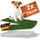 Welpe auf zwei Kunstrasenauflagen über einer Schale, oranges Schild „2x 76cm“, Etikett mit Deutschland-Flagge „Designed in Germany“.