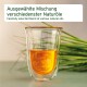 Ein klares Glas mit gold-orangefarbener Flüssigkeit, grünem Gras im Hintergrund und Text über eine Mischung aus natürlichen Ölen.