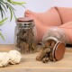 Zwei Glasbehälter gefüllt mit Hundeleckerlis, einer umgekippt und verschüttet Leckerlis, neben einem beigen Seilspielzeug, mit einem rosa Haustierbett im Hintergrund.