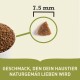 Nahaufnahme von Haustierfutter-Kibble in einer Schüssel, mit einem einzelnen 7,5 mm Stück und Text: "GESCHMACK, DEN DEIN HAUSTIER NATURGEMÄSS LIEBEN WIRD."
