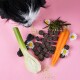 Ein schwarz-weißer Hund schnüffelt an bunten Haustierleckereien, darunter Kaustücke, Sellerie, Karotte und Kräuter, vor einem rosa Hintergrund.