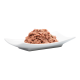 Eine Portion Haustierfutter, die einer glatten, rosafarbenen Paste ähnelt, in einer weißen Schüssel vor einem transparenten Hintergrund präsentiert.