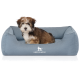Kleiner braun-weiß flauschiger Welpe sitzt in einem blauen rechteckigen Hundebett mit weißem 'KNUFFELWUFF'-Logo.