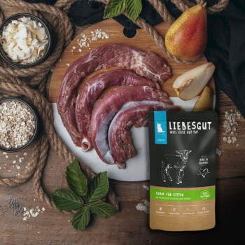 Liebesgut Kitten-Lamm-Futterbeutel neben rohen Lammstücken, Birnenhälften, Haferflocken und Kokosraspeln; Etikett: "LIEBESGUT".