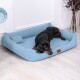 Ein schwarzer Hund, der auf einem hellblauen Hundebett mit einem kleinen Kissen liegt, vor einem hellen, minimalistischen Hintergrund.