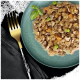 Gros plan d'un bol de nourriture pour animaux avec de la viande hachée, des pois et des carottes, garni de basilic, à côté d'une fourchette dorée sur un tissu sombre.