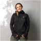 Eine Frau trägt eine schwarze Zip-Jacke mit Kapuze und dem Logo "Dog Gear" auf der linken Brust, vor einem grauen Hintergrund stehend.