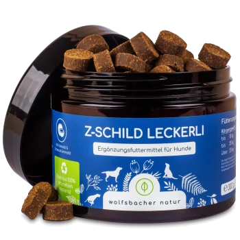 Ein Glas mit Hundeleckerlis, beschriftet mit "Z-SCHILD LECKERLI" in einem blauen und grünen Design, das braune, würfelförmige Snacks enthält.