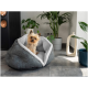 Ein kleiner Yorkshire Terrier sitzt bequem in einem gemütlichen grauen Haustierbett mit weißem Innenraum, umgeben von Zimmerpflanzen und modernem Dekor.