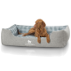 Ein brauner Hund liegt bequem in einem grauen Hundebett mit einem karierten Innenfutter, mit dem Logo "KNUFFELWUFFF" auf der Vorderseite.