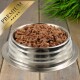 Eine Edelstahlschüssel für Haustierfutter, gefüllt mit hochwertigem Nassfutter für Hunde, mit einer texturierten, fleischigen Mischung, vor einem dekorativen grünen Gras-Hintergrund.