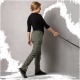 Eine Frau in einem schwarzen Langarmshirt und olivgrünen Cargo-Hosen geht mit einer Hundeleine in ihrer rechten Hand, vor einem grauen Hintergrund.