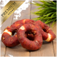 Drei ringförmige Hundeleckerlis, überzogen mit rötlich-braunem Fleisch, auf einer Holzoberfläche mit grünem Gras im Hintergrund.