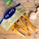 Eine Tüte natürlicher Hundesnacks kippt auf Holz und zeigt kaubare Sticks. Die Tüte ist mit "100% Natürlich" beschriftet und ein Seilspielzeug befindet sich in der Ecke.