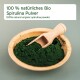 Holzschale mit dunkelgrünem Spirulina-Pulver und Löffel; Etikett: '100% natürliches Bio Spirulina Pulver' und englischer Text.
