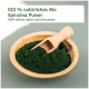 Holzschale mit dunkelgrünem Spirulina-Pulver und Löffel; Etikett: '100% natürliches Bio Spirulina Pulver' und englischer Text.
