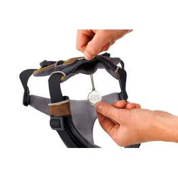 Eine Person passt ein grau-schwarzes Hundegeschirr an und hält ein Metallschild, auf dem "RUFF WEAR 888-783-3962" steht.