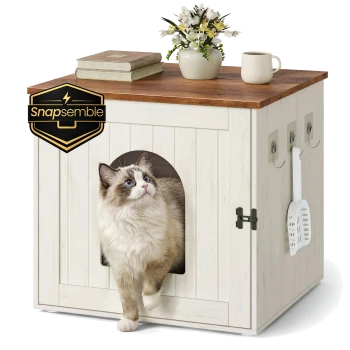 Ragdoll-Katze steigt aus einem weißen Holz-Katzentoilettenschrank mit seitlicher Schaufel; Bücher, Vase und Tasse obenauf; 'Snapssemble'-Logo.