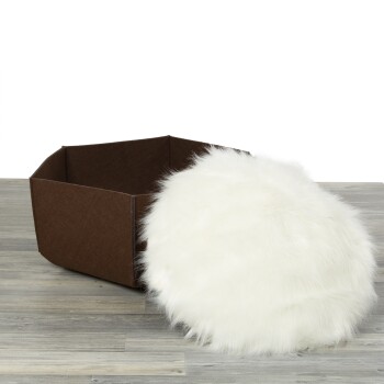 Ein braunes Haustierbett mit einem weichen, flauschigen weißen Kissen daneben, auf einem hellen Holzboden.