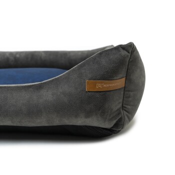 Graues Hundebett mit einem blauen Kissen und einem Lederetikett, auf dem "Rex Production" steht.