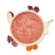 Weiße Schüssel mit rosa Feuchtfutter aus gemahlenem Fleisch, umgeben von einer Apfelscheibe, einer Birnenhälfte, Karottenscheiben und rohen Fleischstücken.