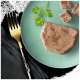 Une tranche de nourriture pour animaux sur une assiette vert clair, accompagnée d'une branche de persil et de petits cubes de la même nourriture, avec une fourchette dorée à proximité.