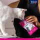Eine weiße Katze schnüffelt an einer pinken Tüte Vitakraft Choupette Katzenleckerlis, die von einer Person gehalten wird, und zeigt das Branding und Design des Produkts.