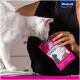 Un chat blanc renifle un sac rose de friandises pour chats Vitakraft Choupette tenu par une personne, mettant en valeur la marque et le design du produit.
