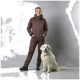Eine Person in einem braunen isolierten Overall steht neben einem freundlichen golden retriever vor einem grauen Hintergrund.