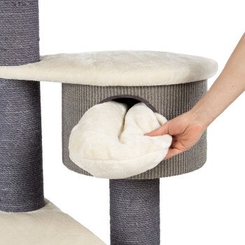 Eine Hand zieht ein weiches, weißes Plüschbett aus einem gemütlichen, grauen Katzenbaum mit einem runden Versteck und einer flachen Oberseite.