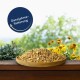 Eine Holzschüssel mit Haustierfutter auf einer Holzoberfläche, umgeben von grünen Pflanzen und gelben Blumen, mit einem blauen Etikett "Ganzjahresfütterung."