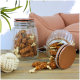 Ein Glasbehälter gefüllt mit Hundeleckerlis in Knochenform, mit einigen Leckerlis, die daneben gefallen sind, neben einem Seilspielzeug und einem rosa Sofa.