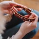 Hände halten ein braunes Lederhundehalsband mit silbernen Herznieten, runden Nieten und Metallschnalle