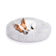 Ein kleiner, schlafender Hund mit braun-weißer Fellfarbe, der sich auf einem flauschigen grauen runden Haustierbett zusammenrollt.