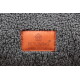 Grauem Sherpa-Stoff eines Haustierbetts mit orangefarbenem Lederetikett mit der Aufschrift 'PETLIVING place to enjoy' und Pfoten-im-Haus-Logo.