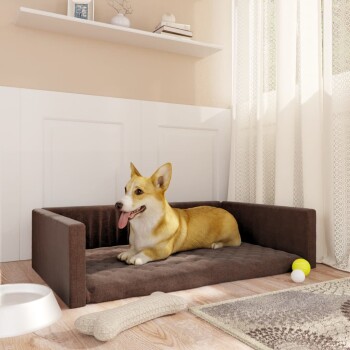 Ein entspannter Corgi liegt auf einem braunen Tierbett in einem gemütlichen Raum, mit einer weißen Futterschüssel, einem Kauspielzeug und bunten Bällen in der Nähe.
