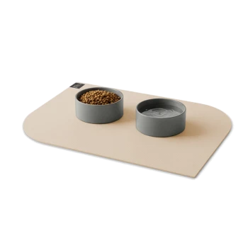 Beige Haustier-Futtermatte mit zwei grauen Schüsseln – eine mit Trockenfutter, eine mit Wasser – kleines schwarzes Markenschild oben links.