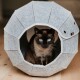 Eine Siamkatze mit auffälligen blauen Augen sitzt in einer grauen Filzhaustierhöhle, die ein achteckiges Design und ein kleines Logo an der Seite hat.