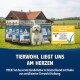 Kleiner weißer Hund sitzt auf Gras mit M!EAT Hundefuttertüten und einem Schild über zertifizierten Tierschutz in deutscher Sprache.