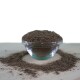 Eine klare Glasschüssel gefüllt mit einem feinen, dunkelbraunen Pulver, umgeben von einer Staubschicht desselben Pulvers auf einer hellen Oberfläche.