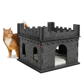 Eine verspielte orangefarbene Katze steht neben einem grauen Filz-Katzenhaus in Form einer Burg mit gewölbten Eingängen und einem weichen Innenraum.