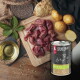 Dose LIEBESGUT-Hundefutter mit der Aufschrift 'Schaf für Hunde' neben rohen Lammstücken, Kartoffeln, Öl und Samen auf einem Holzbrett.