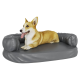 Ein entspannter Corgi liegt auf einem grauen Hundebett mit erhöhten Seiten und zeigt seinen verspielten Ausdruck mit herausgestreckter Zunge.