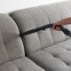 Eine Hand hält eine Staubsaugerdüse und reinigt ein hellgraues, gepolstertes Sofa.
