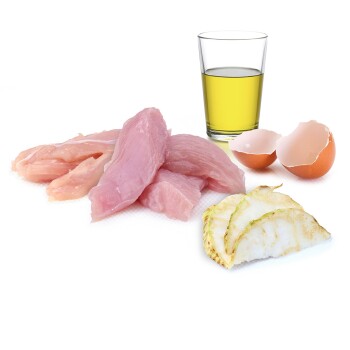 Rohe Hähnchenfilets, ein Glas Olivenöl, Eierschalen und Scheiben eines Gemüses auf einem weißen Hintergrund.