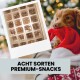 Hund hält einen roten Weihnachtsmannhut mit Foto von verschiedenen Premium-Hundesnacks mit der Aufschrift „Acht Sorten Premium-Snacks“ auf Deutsch.