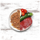 Ein geteilter Teller mit Haustierfutter auf der linken Seite und frischen Zutaten – rohem Steak, Zucchini, Kirschtomaten und Apfelscheibe – auf der rechten Seite.