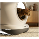 Bengalkatze lugt aus einer modernen weißen automatischen Katzentoilette auf einem Teppich, dahinter ein Holzschrank und dekorative Vasen.