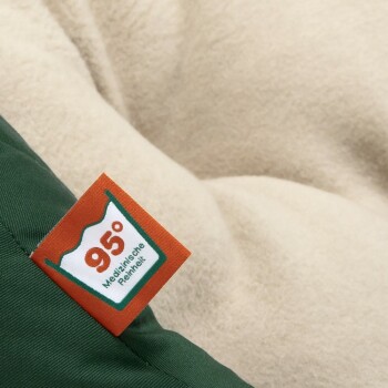 Eine Nahaufnahme eines Haustierbettes mit einem grünen Stoffrand und einem weichen beigen Innenraum, mit einem Etikett, das "95° Medizinische Reinheit" liest.
